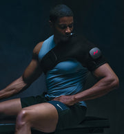 Person wearing a black and blue athletic outfit wearing a venom 2 shoulder sitting against a dark background.