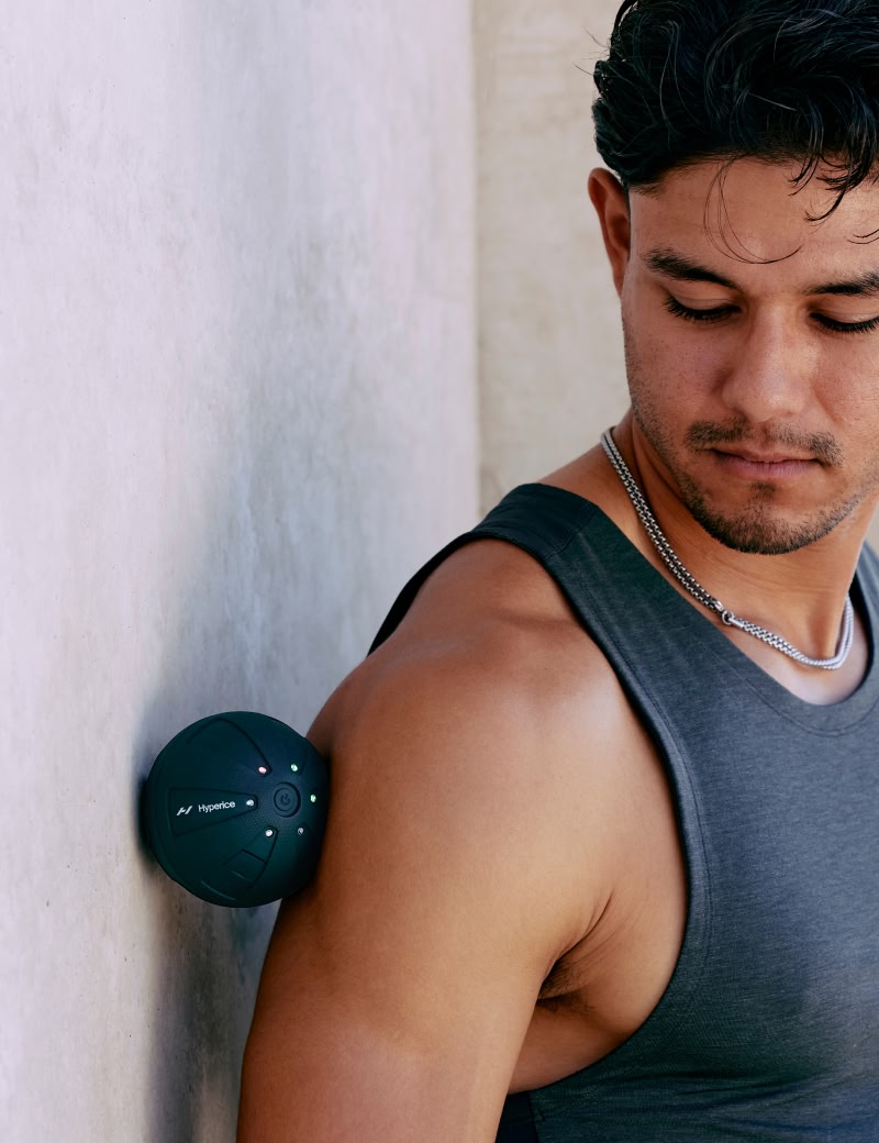 Man in a gray tank top leaning against a wall with a hypersphere go between him.