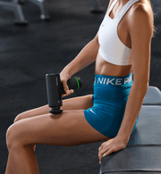 Person using a Hypervolt Go 3 massage gun in a gym setting, wearing Nike Pro shorts.