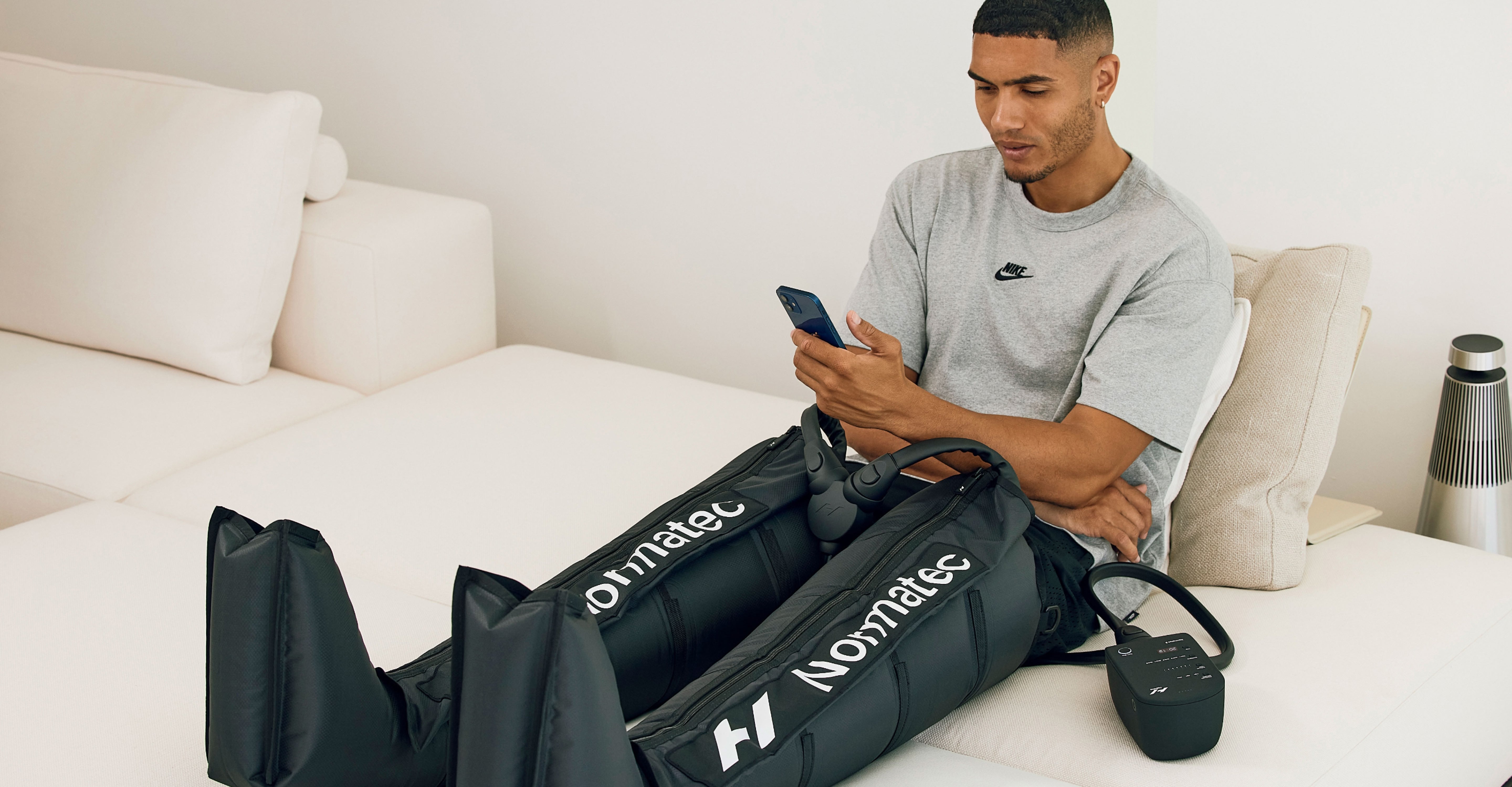 Man sitting on a bed using a smartphone while using the normatec 3 leg system