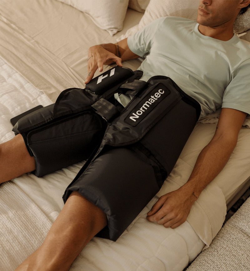 Person using a Normatec elite hips compression device on their hips in a bedroom setting.