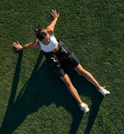 A person sitting down on a grassy field with arms outstretched wearing normatec elite hips