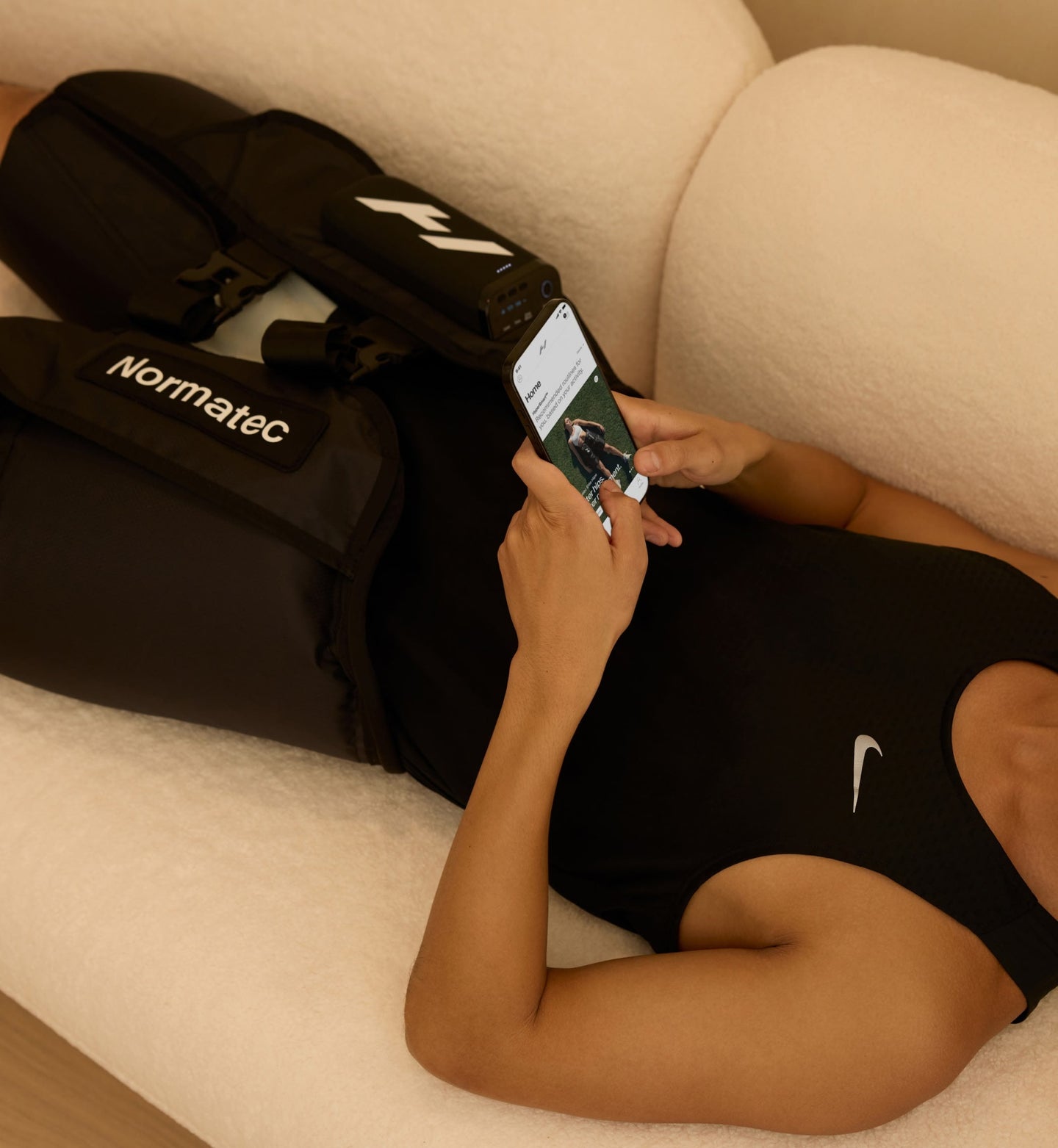 Person laying on a couch using a smartphone with Normatec elite hips on