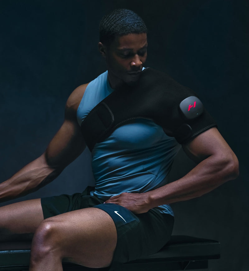 Person wearing a black and blue athletic outfit wearing a venom 2 shoulder sitting against a dark background.